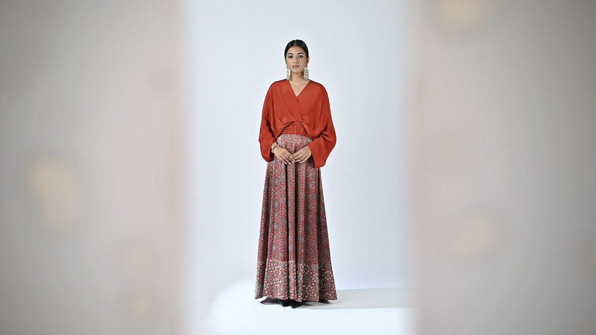 Red ajrakh embellished gown for karwa chauth eve preparation — rust-red draped top and red ajrakh printed skirt, full outfit on a model