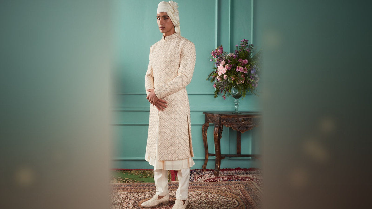 Ivory groom sherwani with all-over zardosi embroidery worn open over a kurta with a pearl turban, full length