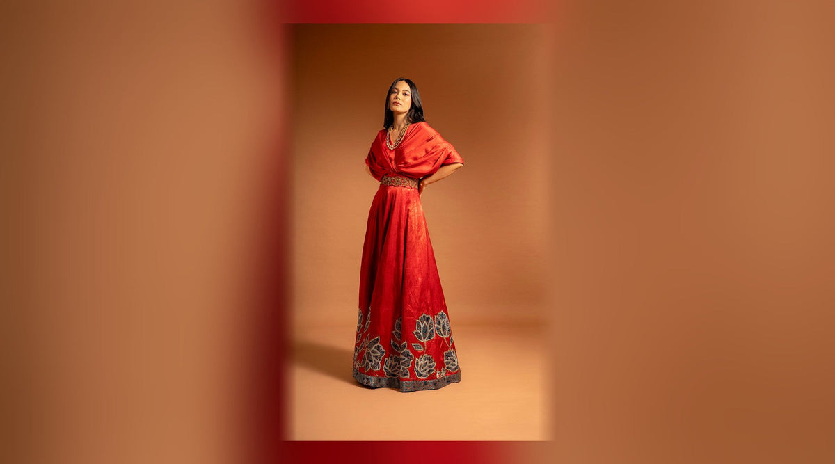 Red ajrakh embroidered gown for karwa chauth eve outfits — bright red draped gown with gold embroidered belt and floral hem, full outfit on a model